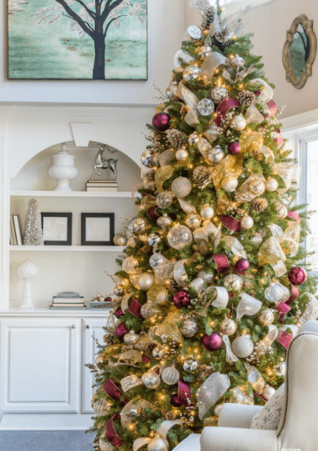 lush Christmas tree decor with lots of lights, metallic ornaments, white and burgundy ribbons and pinecones