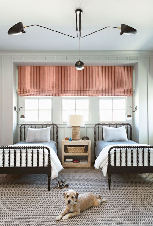 a chic shared guest bedroom with a tirple window covered with a coral shade and a printed rug