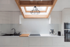 03 The kitchen is done with sleek white cabinets, wooden touches, black items for a contrast and a skylight