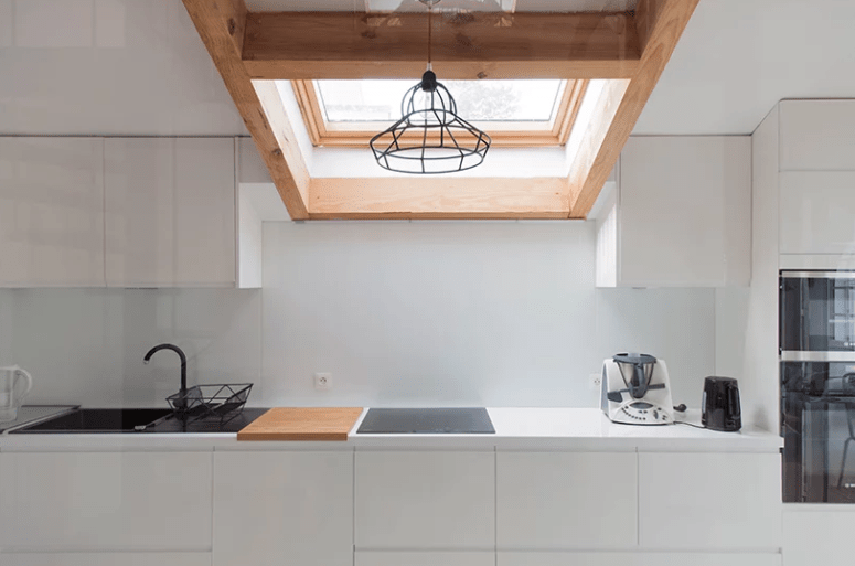 The kitchen is done with sleek white cabinets, wooden touches, black items for a contrast and a skylight