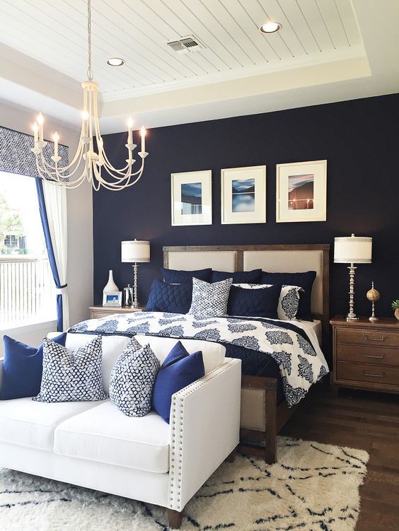a bedroom with a navy statement wall, navy and white bedding and a creamy couch with navy pillows