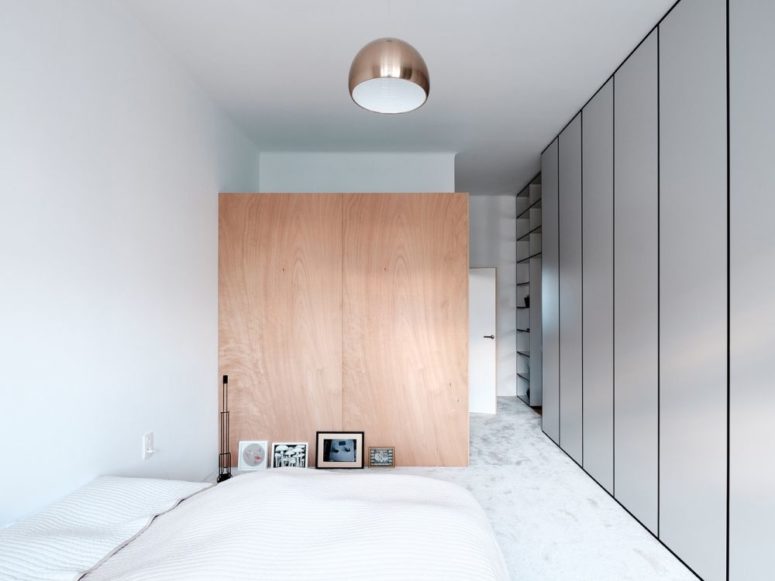 The bedroom is decorated in neutrals, with a wooden space divider and closed storage units