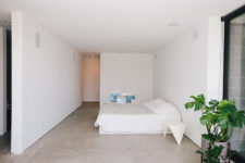 05 The master bedroom is all-white, with a large bed and some blue artworks plus potted plants