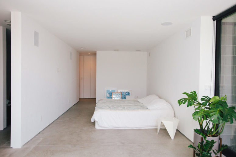 The master bedroom is all-white, with a large bed and some blue artworks plus potted plants