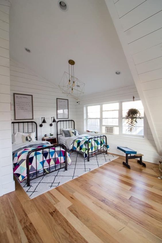 a cozy and large attic bedroomwith two beds and colorful textiles plus geometric ceiling lamps