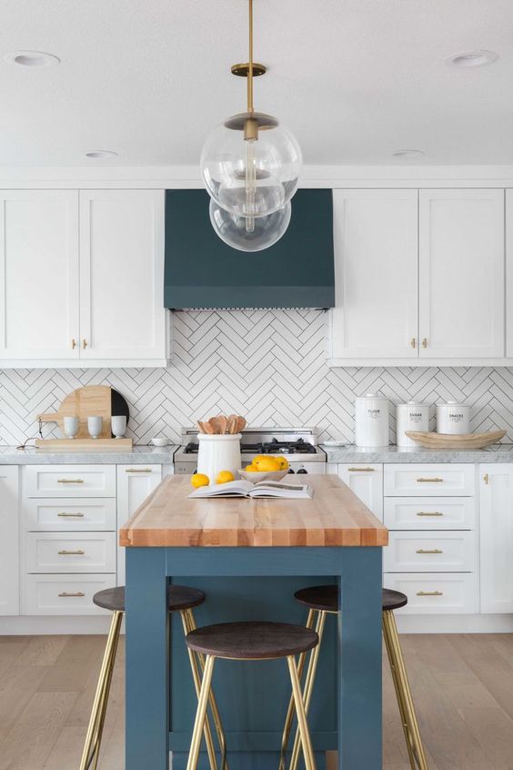 a white kitchen with a herringbone tile backsplash and a navy hood and kitchen island with a wooden countertop