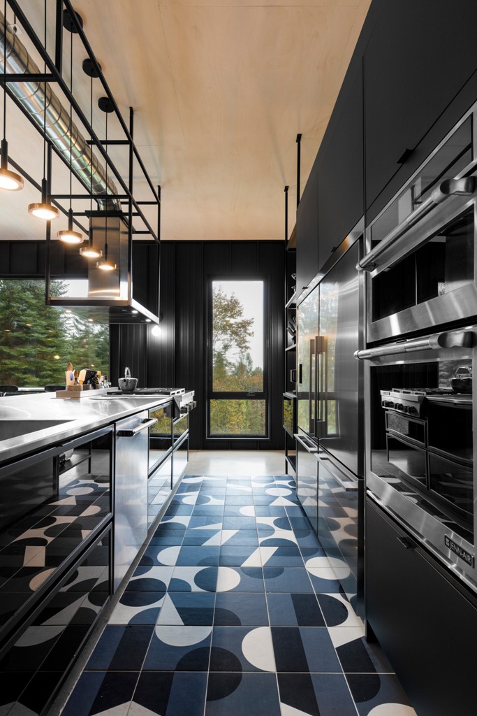 A moody kitchen is done with black sleek cabinets, a mosaic tile floor in black and white