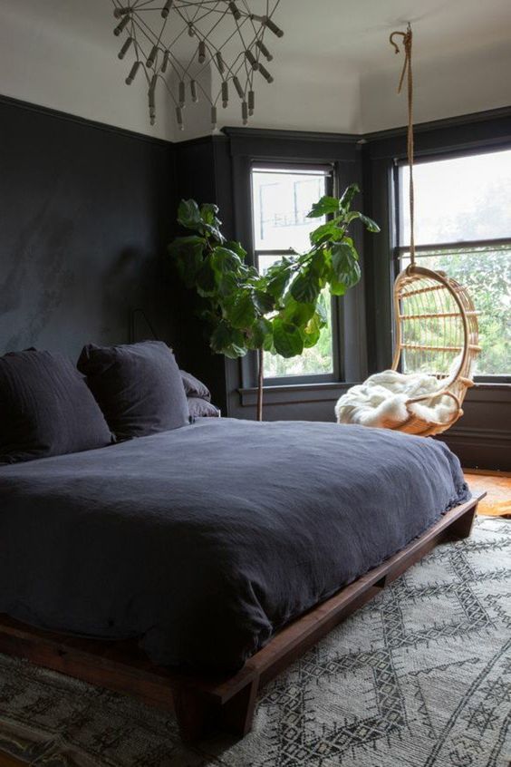 a dark bedroom is filled with natural light, styled with dark bedding and neutral textiles