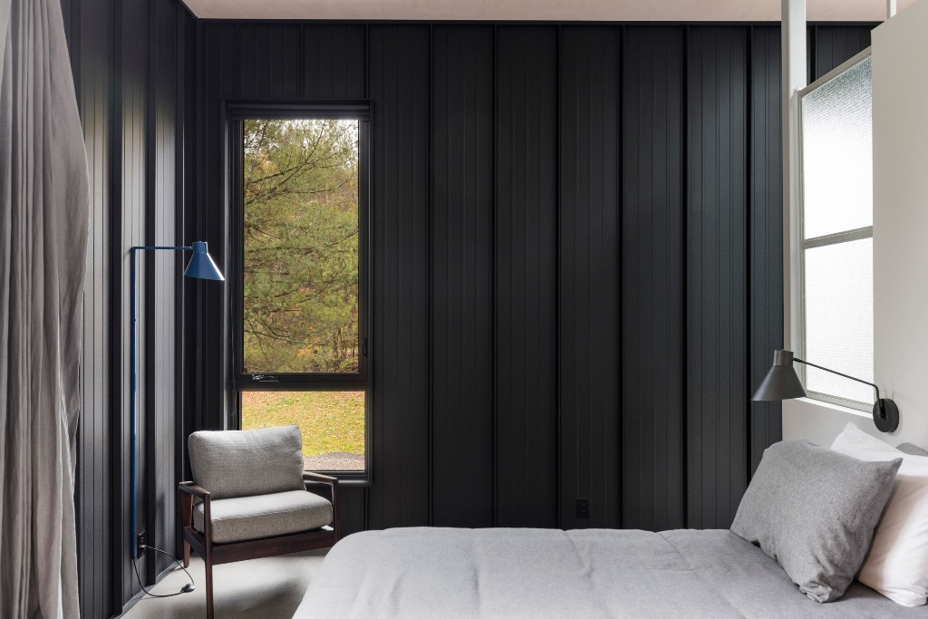 The bedroom also features black wood clad walls, windows fill the space with natural light