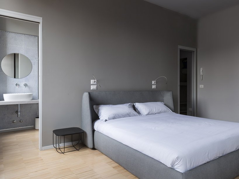 The bedroom is done in the shades of grey, with grey walls and a grey upholstered bed and a duo of metal bedside tables
