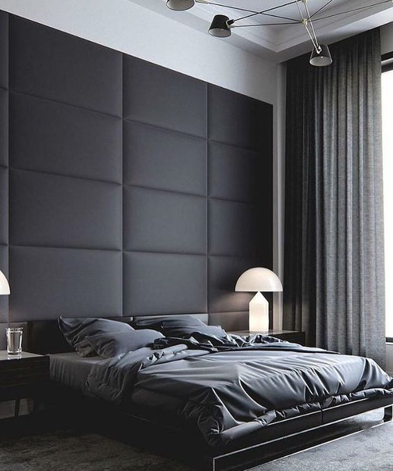 a minimalist neutral bedroom with a black upholstered statement wall and dark bedding looks very comfy