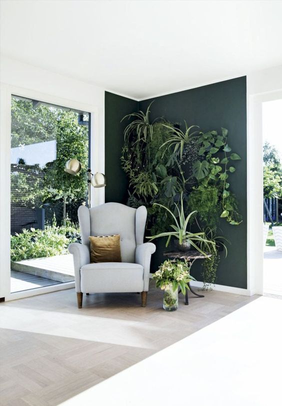 a dark green statement wall with lots of fresh potted plants and a little chair to make up a cozy nook