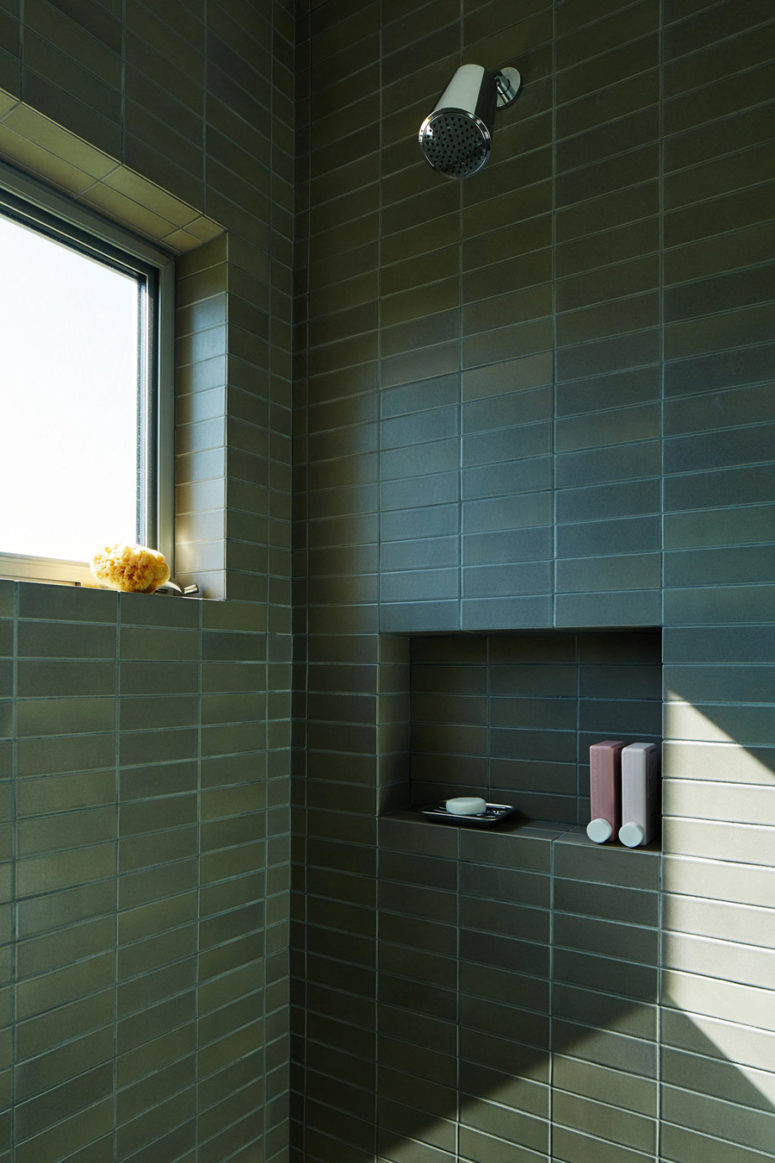 The bathroom features a shower with matte dark green tiles that are long and narrow