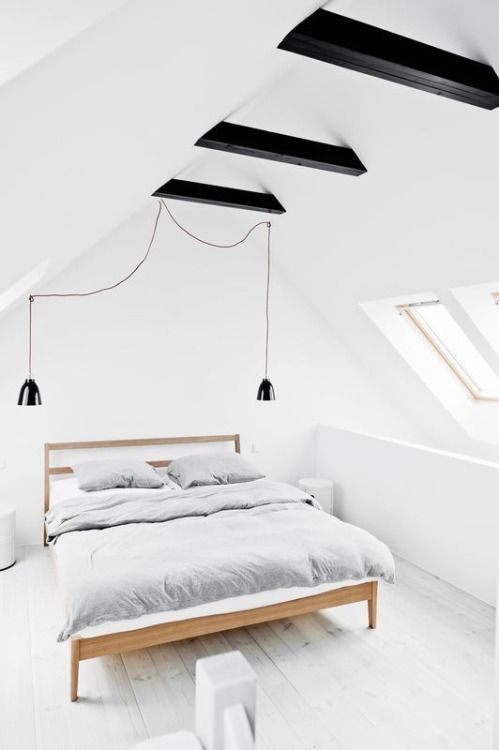 a light-filled and airy attic bedroom with black ceiling beams and black pendant lamps for more drama