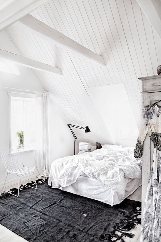 a totally white attic bedroom with a floating bed, much light and a single black rug for a contrast