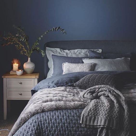 a very cozy bedroom with a navy wall and navy and white bedding and blankets