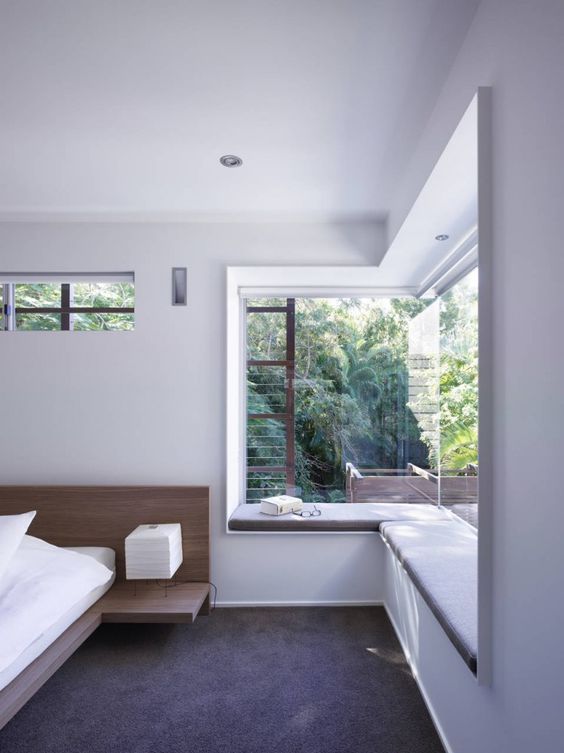 a minimalist bedroom with an upholstered windowsill as a daybed or a seat is a cool idea to catch the views