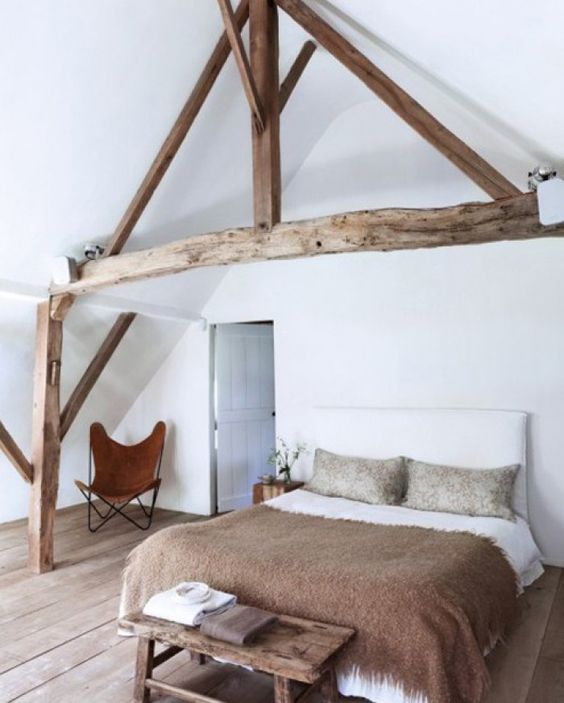An attic space styled with only a comfy bed, a rustic bench and a leather butterfly chair