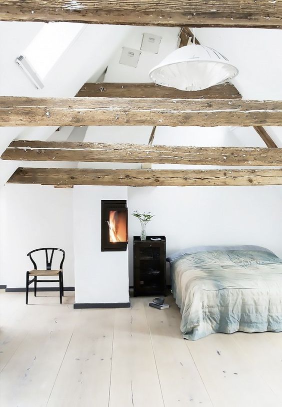 A cozy light filled bedroom with wooden beams on the ceiling and a warming up hearth by the bed