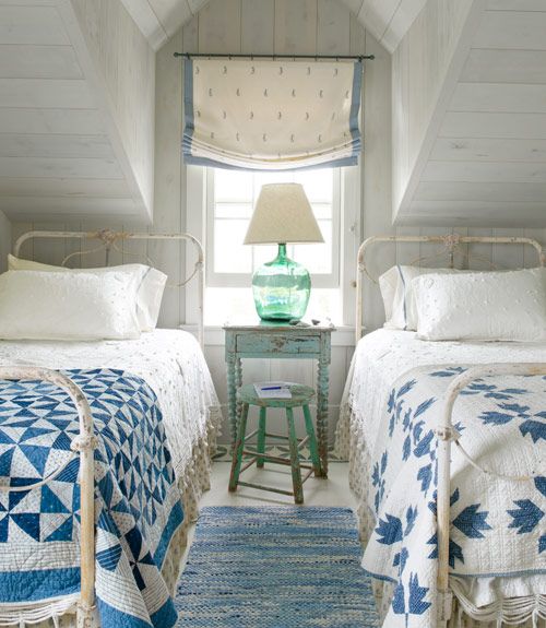 a small attic oceanside guest bedroom with two beds and some shabby chic furniture
