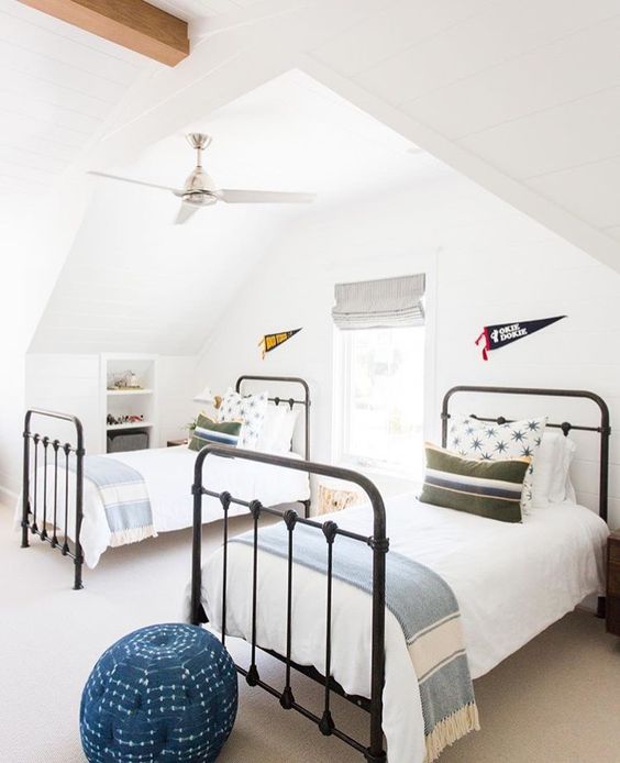 a stylish attic guest bedroom with two beds, a single window with shades and blue touches