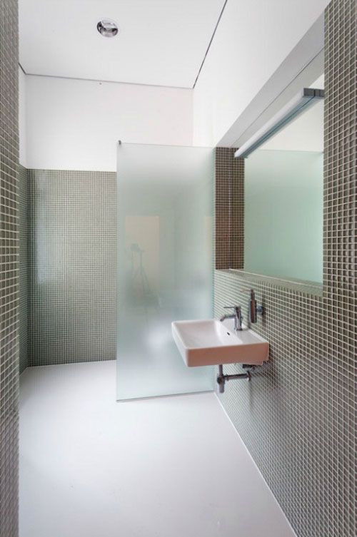 a stylish minimalist bathroom with grey tiles and white grout and a frosted glass space divider for the toilet