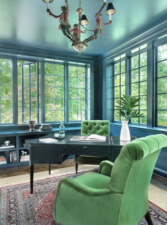 A vintage inspired elegant blue home office accented with a black desk and green velvet chairs