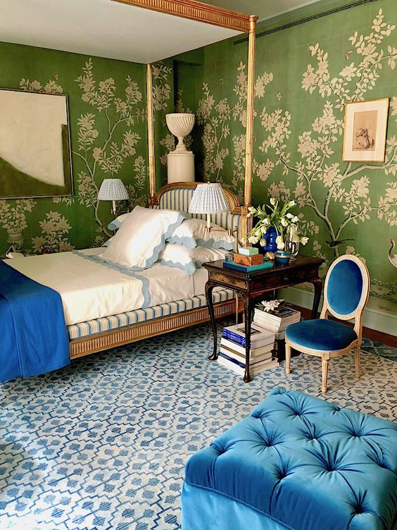 a sophisticated bedroom with botanical print wallpaper and medium blue accents - a chair, an ottoman and a blanket