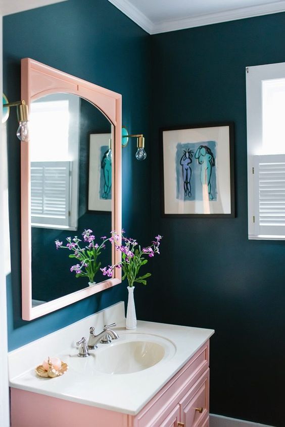 a navy bathroom with a blush mirror and a blush vanity plus brass touches here and there