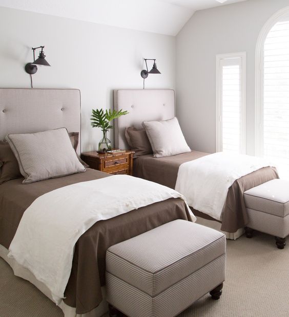a stylish modern guest bedroom with two beds, storag eottomans and some wall lamps