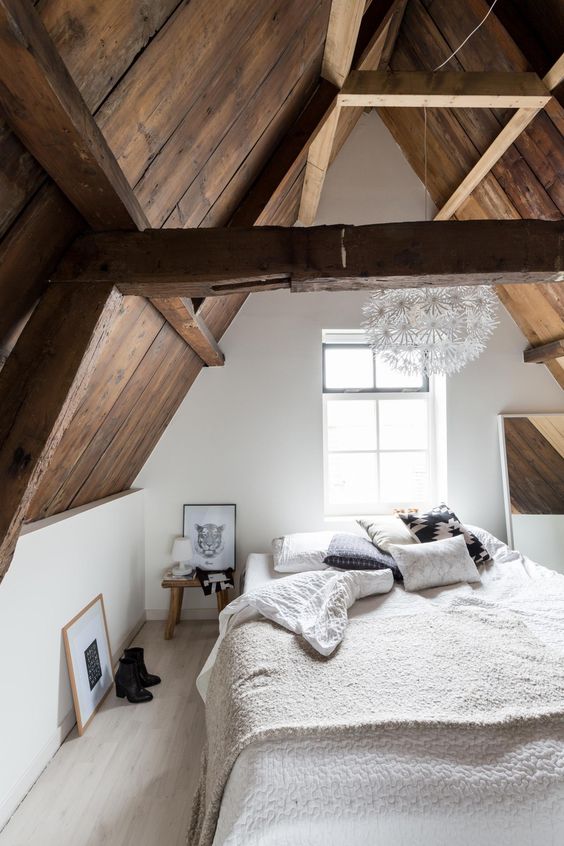 a large bed, a mirror and wooden bedside tables that echo with the sloped ceiling and beams