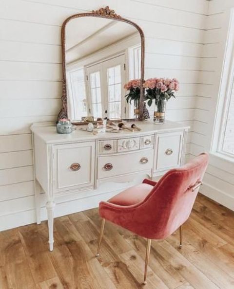 a vintage vanity and a pink upholstered chair by it as a colorful touch and a seating piece