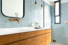 a beautiful coastal bathroom clad with light blue hex tiles, a large floating vanity, touches of black and brass