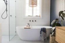 a beautiful contemporary coastal bathroom with a navy wooden wall, white skinny tiles, a woven lamp and a plant in a basket