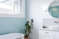 a coastal bathroom with blue herringbone and white marble tiles, a shiplap wall, a white vanity and an oval tub, a side table