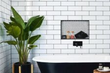 a contrasting bathroom with white subway tiles and black hex ones, a black clawfoot tub and wooden furniture