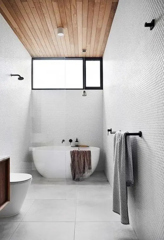 a dove grey bathroom with penny and large scale tiles, a wooden ceiling, an oval tub and black fixtures is very stylish
