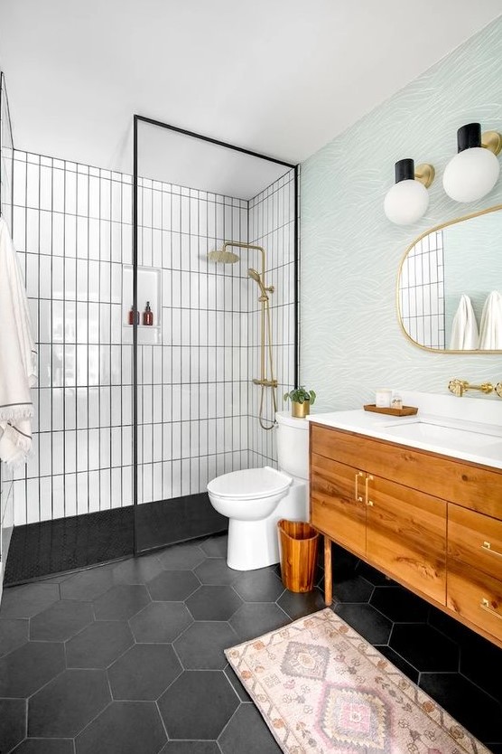 A mid century modern bathroom with white skinny and black hex tiles, a stained vanity, a blue accent wall, gold fixtures