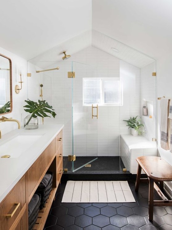 A mid century modern bathroom with white skinny and black hex tiles, a stained vanity and a bench, gold fixtures