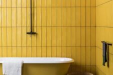 a minimal bathroom with mustard tile walls and a mustard bathtub, a dark stone tile floor and baskets