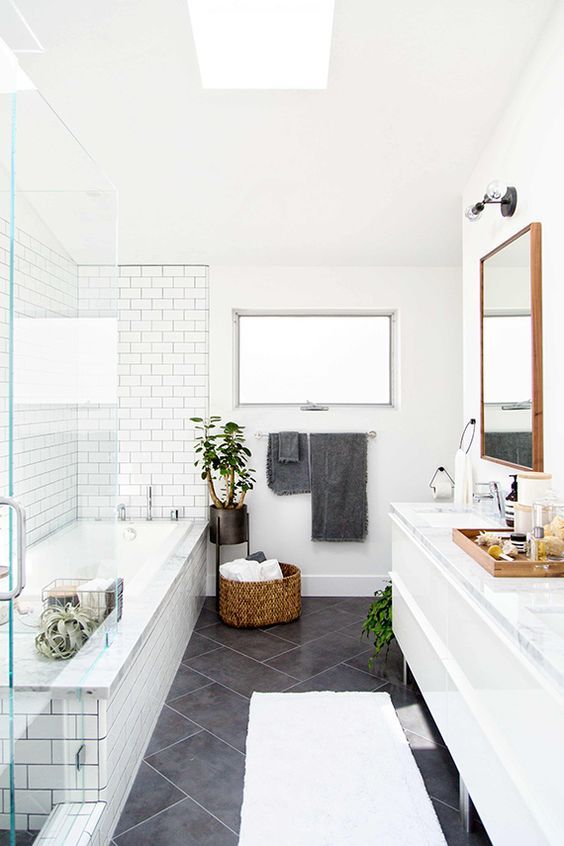 a modern bathroom with grey square and white subway tiles, a large vanity, potted greenery, a basket with towels