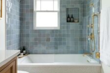 a modern bathroom with penny tiles and blue zellige ones around the tub, a timber vanity, gold and brass fixtures