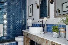 a modern beach bathroom with a shower clad with bright blue tiles, a round sink, vintage faucets and a gorgeous weathered wood vanity