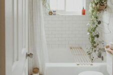 a neutral boho bathroom with white penny and subway tiles, a bathtub, potted greenery, a stained stool is welcoming