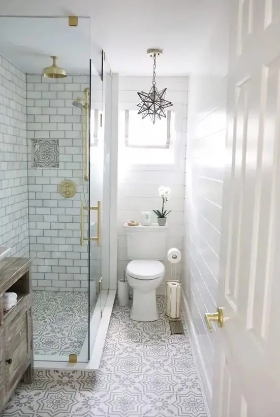 A neutral small bathroom with beadboard, printed tiles, subway tiles in the shower, gold touches and a star shaped chandelier
