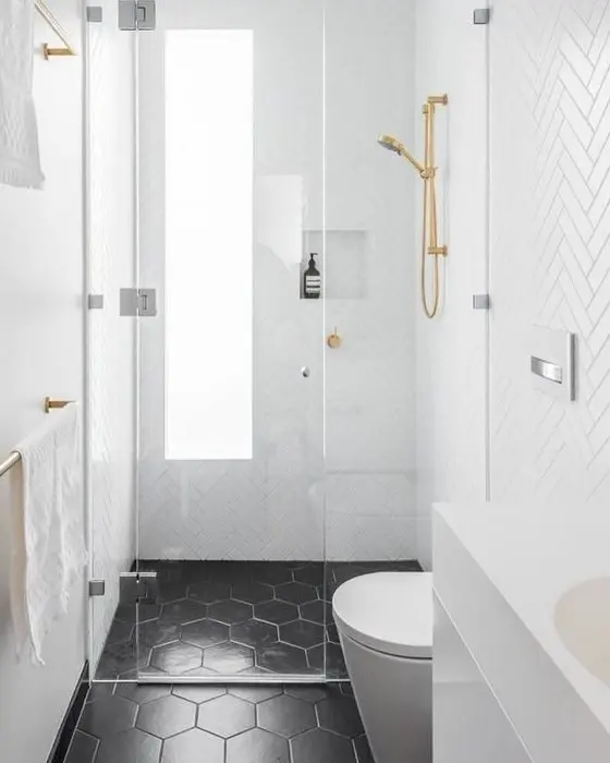 a small bathroom with white herringbone tiles and black hex ones, with a frosted glass window and gold fixtures