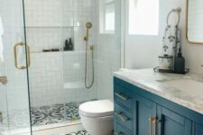 a small bright bathroom with white tiles in the shower, printed tiles on the floor, a navy vanity and brass fixtures