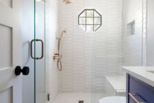 a tiny bathroom with white and printed tiles, a navy vanity, white appliances, brass fixtures and black touches