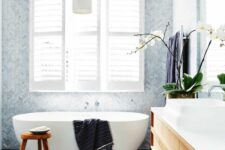 a welcoming modern bathroom with black large scale and light blue herringbone tiles, an oval tub, a timber vanity and dark towels
