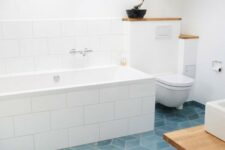 an airy attic bathroom with blue geometric tile floor, large scale subway tiles and white appliances